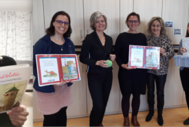 Sie sehen das Team der Pädagogischen Hochschule Tirol am Tiroler Vorlesetag. Es werden lächelnd Bücher gezeigt.